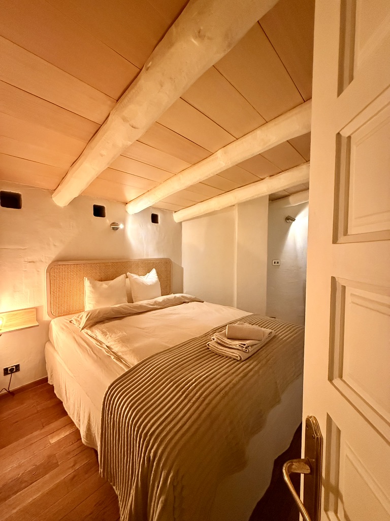 Schlafzimmer mit Rattan-Kopfteil und Holzbalkendecke